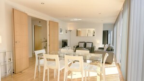 A modern living room with a glass dining table, white chairs, a sofa, and a large window. - Roomspace Apartments -Watling Street (London)