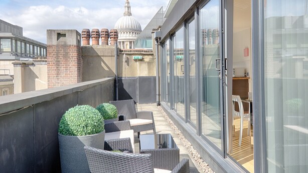 A rooftop terrace with wicker furniture, a glass door leading to an indoor area, and a view of a dome in the background. - Roomspace Apartments -Watling Street (London)