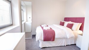 A bedroom with a bed, white bedding, a pink headboard, and a window with blinds. - Roomspace Apartments -Watling Street (London)