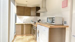 A modern kitchen with wooden cabinets, a built-in microwave, a washing machine, and a stainless steel sink. - Roomspace Apartments -Watling Street (London)