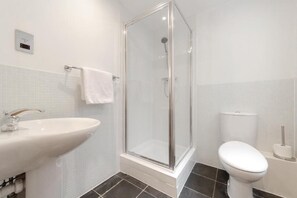 A bathroom with a glass-enclosed shower, a white sink, and a toilet. - Roomspace Apartments -Watling Street (London)