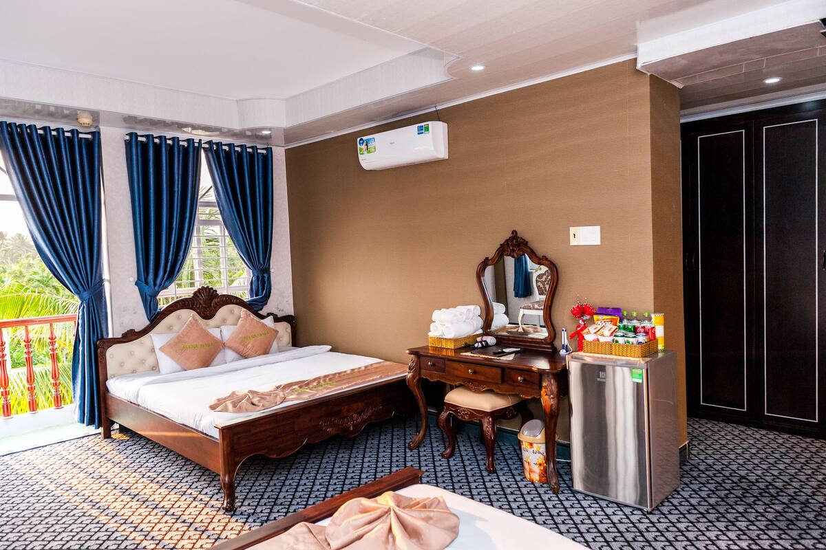 A hotel room with a bed, a dresser, a mirror, an air conditioner, and a refrigerator.