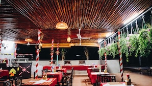 An outdoor restaurant with bamboo ceiling, red and white striped columns, hanging plants, and tables set for dining. - Mui Ne Alena Bungalow Hotel (Mui Ne)