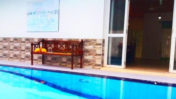 A swimming pool with a wooden bench and stone wall. - The triple bbb villa (Negombo)