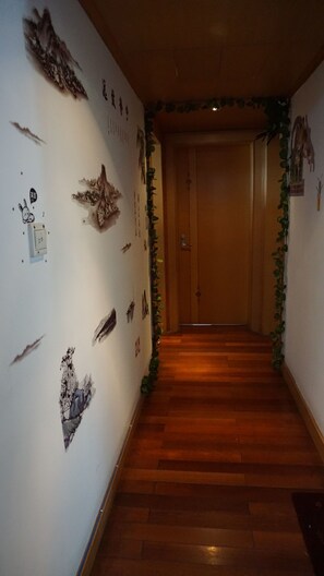 A hallway with wooden flooring, a closed door at the end, and walls decorated with various wall art and a small plant. - Shanghai Mofang Style Girls' Hostel (Shanghai)