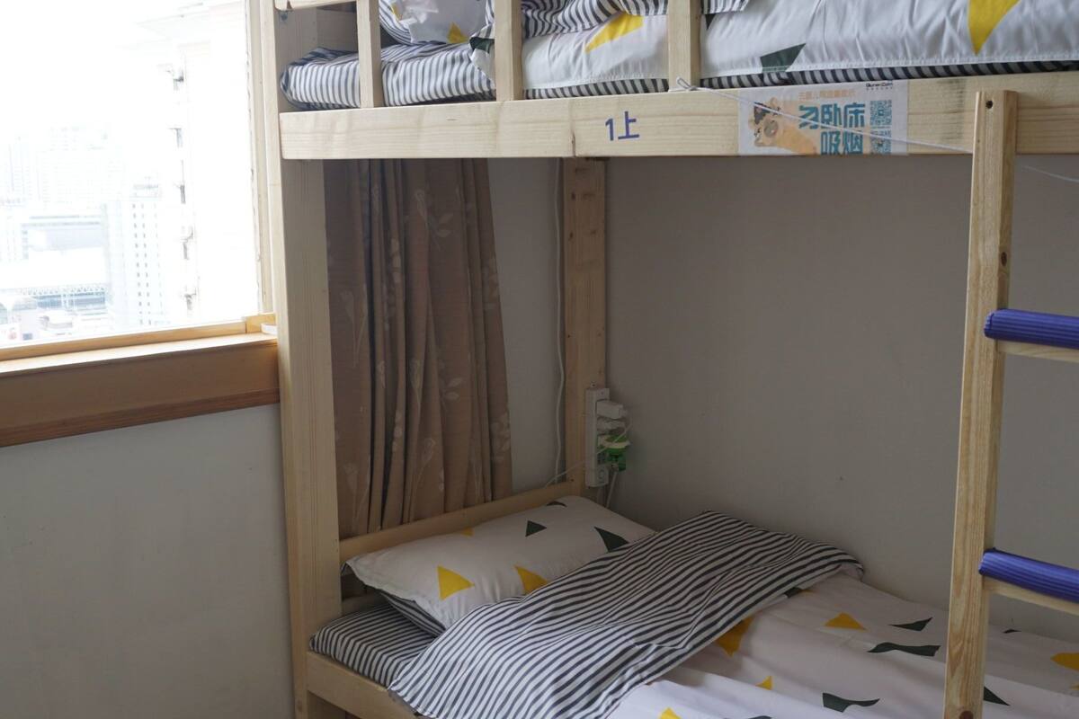 A bunk bed room with a window, curtains, and an air conditioning unit.