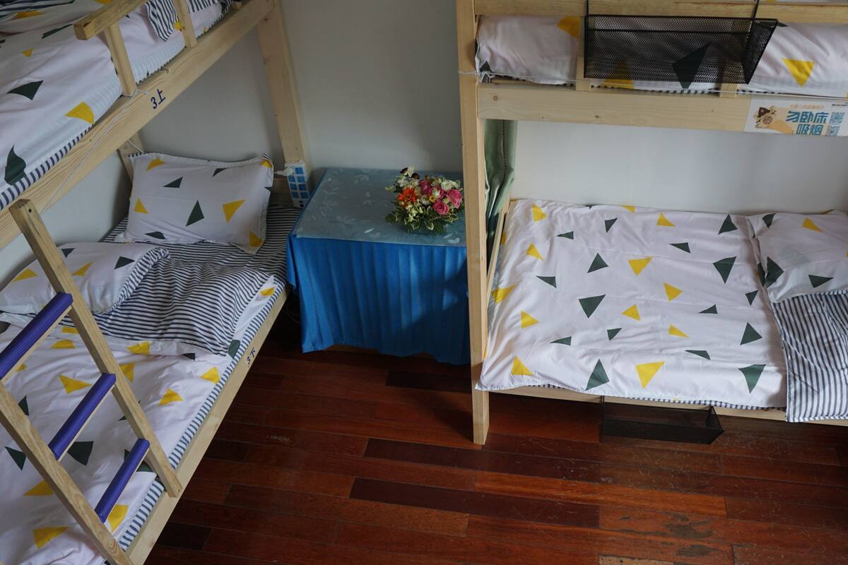 A dormitory room with bunk beds, a small table with a blue tablecloth, and a floral arrangement.