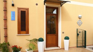 A building entrance with a wooden door, a sign reading "B&B", and potted plants. - Coralia Bed and Breakfast (San Vito Lo Capo)