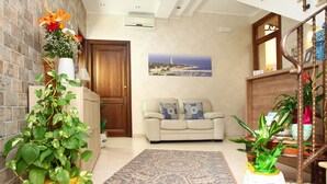 A living room with a sofa, a patterned rug, and two potted plants. - Coralia Bed and Breakfast (San Vito Lo Capo)