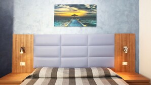 A bedroom with a bed, a headboard, and a wall-mounted picture of a sunset over the ocean. - Coralia Bed and Breakfast (San Vito Lo Capo)