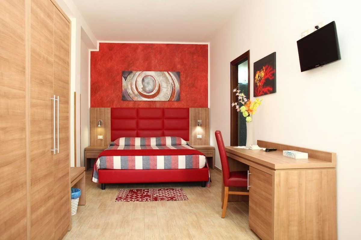 Une chambre moderne avec un lit rouge, une armoire en bois et un bureau avec une chaise.