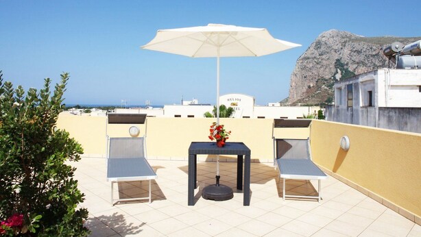 A rooftop terrace with a table, two chairs, and a white umbrella. A sign for "Helios Hotel" is visible in the background. - Coralia Bed and Breakfast (San Vito Lo Capo)