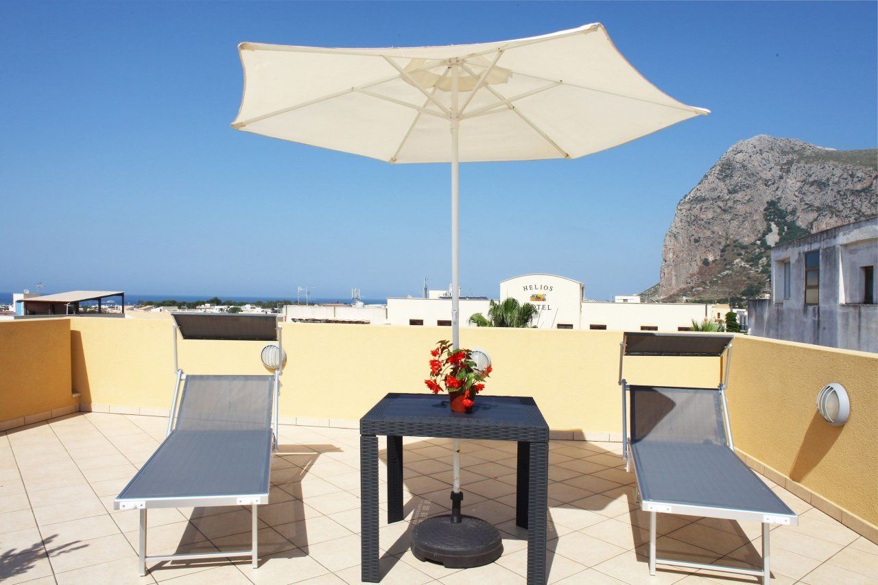 Une terrasse sur le toit avec deux chaises longues, une table ornée d’un vase de fleurs et un grand parasol.