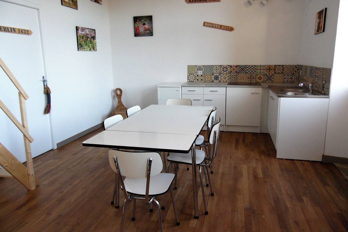 A compact kitchen with a dining area, featuring a white table, chairs, and a wooden staircase.