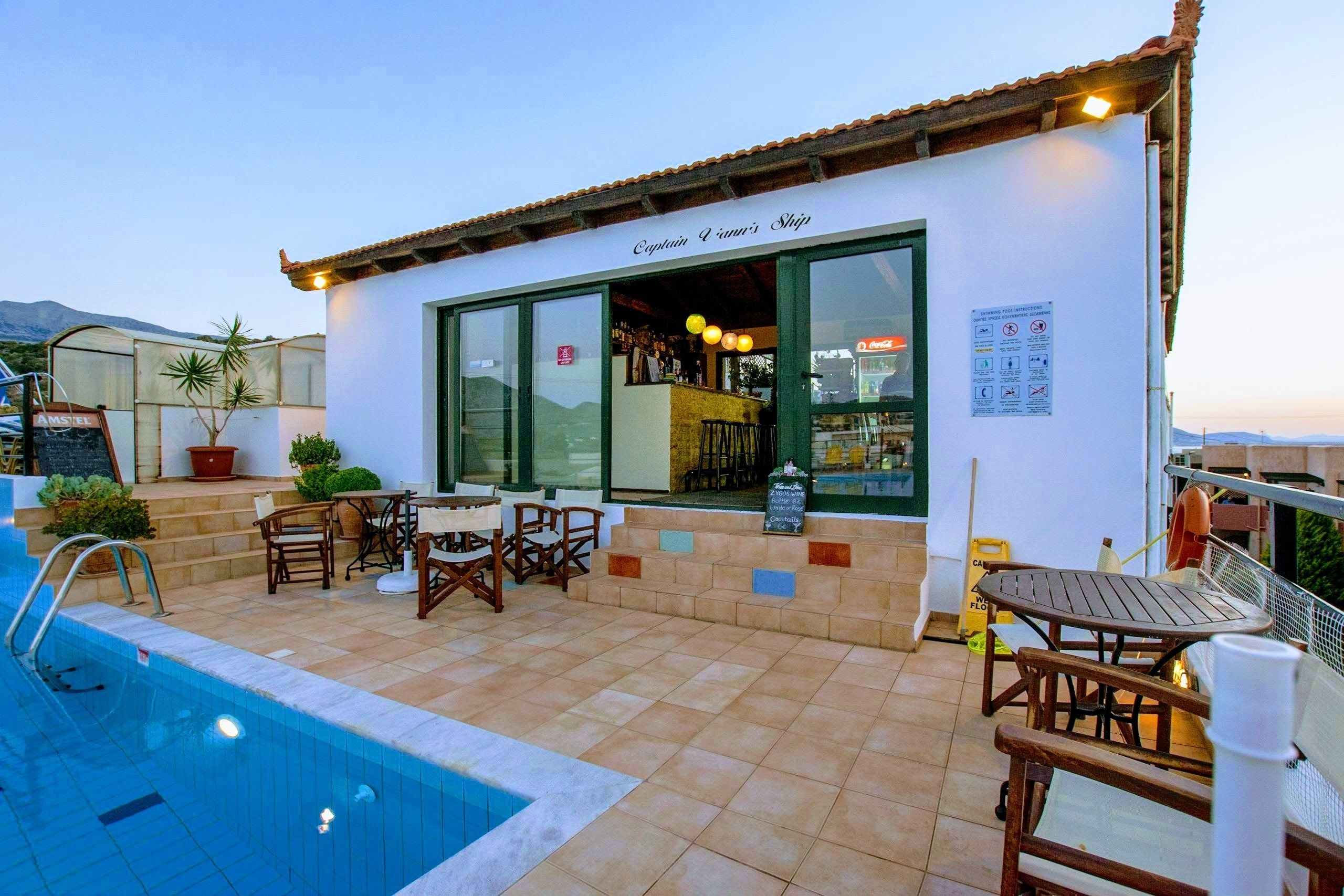 A poolside area with a bar named "Captain & Mrs's Ship," outdoor seating, and a view of the mountains.