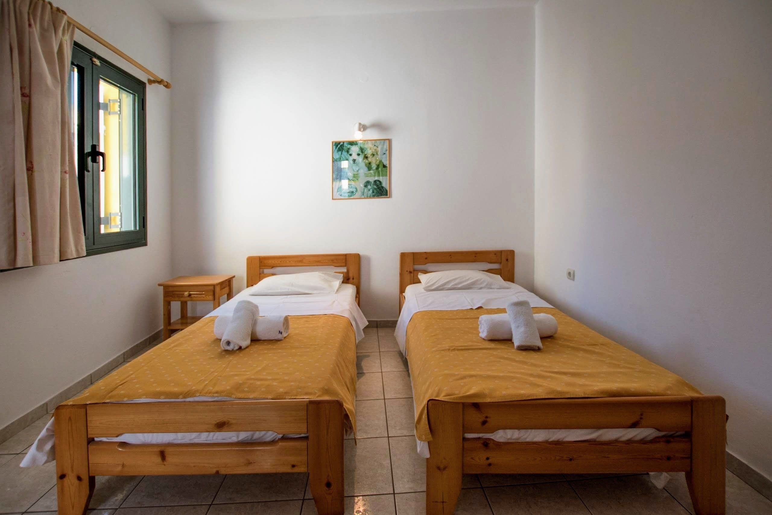 Een kamer met twee houten bedden, een klein nachtkastje en een raam met gordijnen.