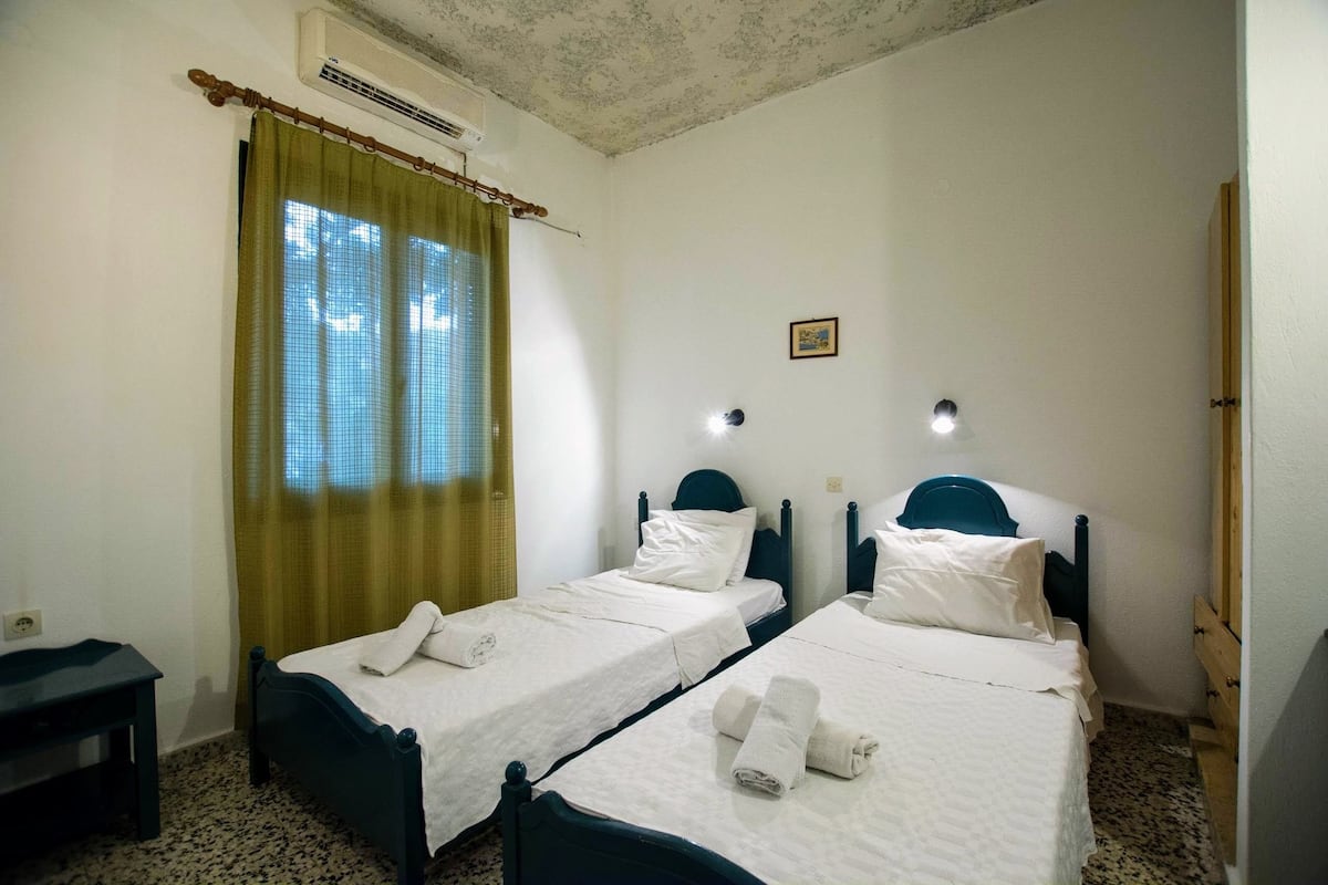 A room with two single beds, a small table, and a window with a curtain.