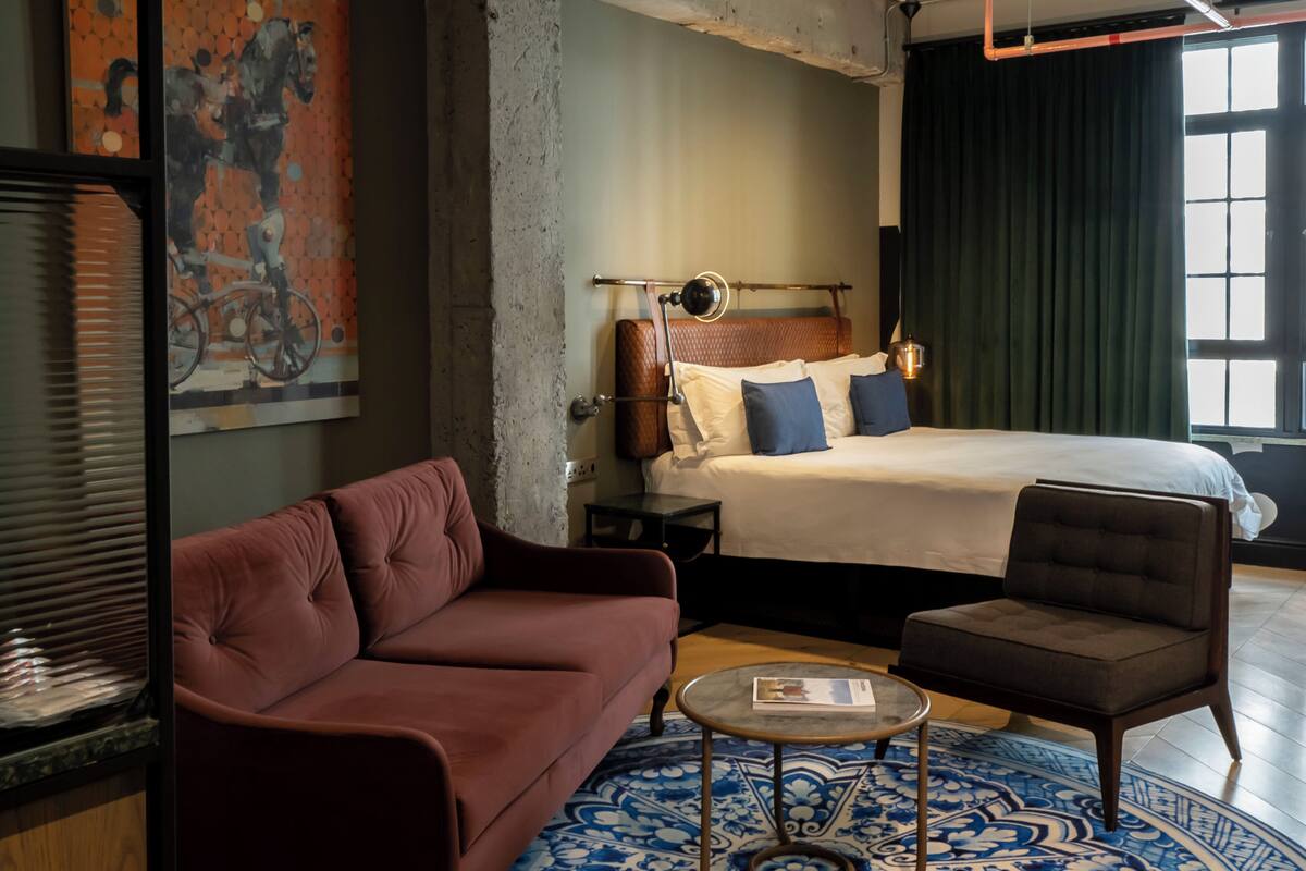 A hotel room with a large bed, a red sofa, a small table, and a patterned rug.