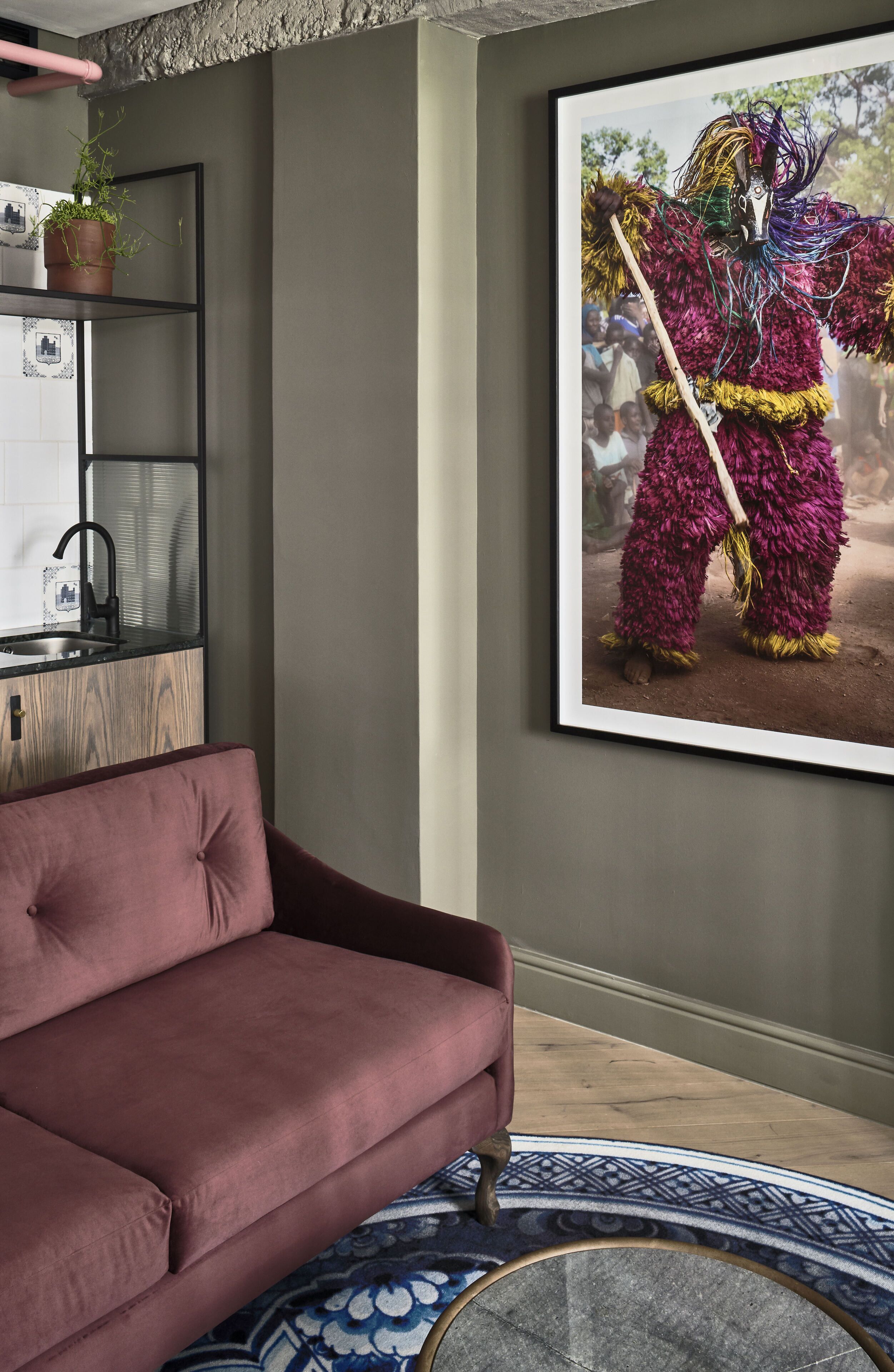 Una sala moderna con pared verde oscuro, un mueble de madera, un sofá rosa y una fotografía enmarcada de un traje de baile tradicional colorido.