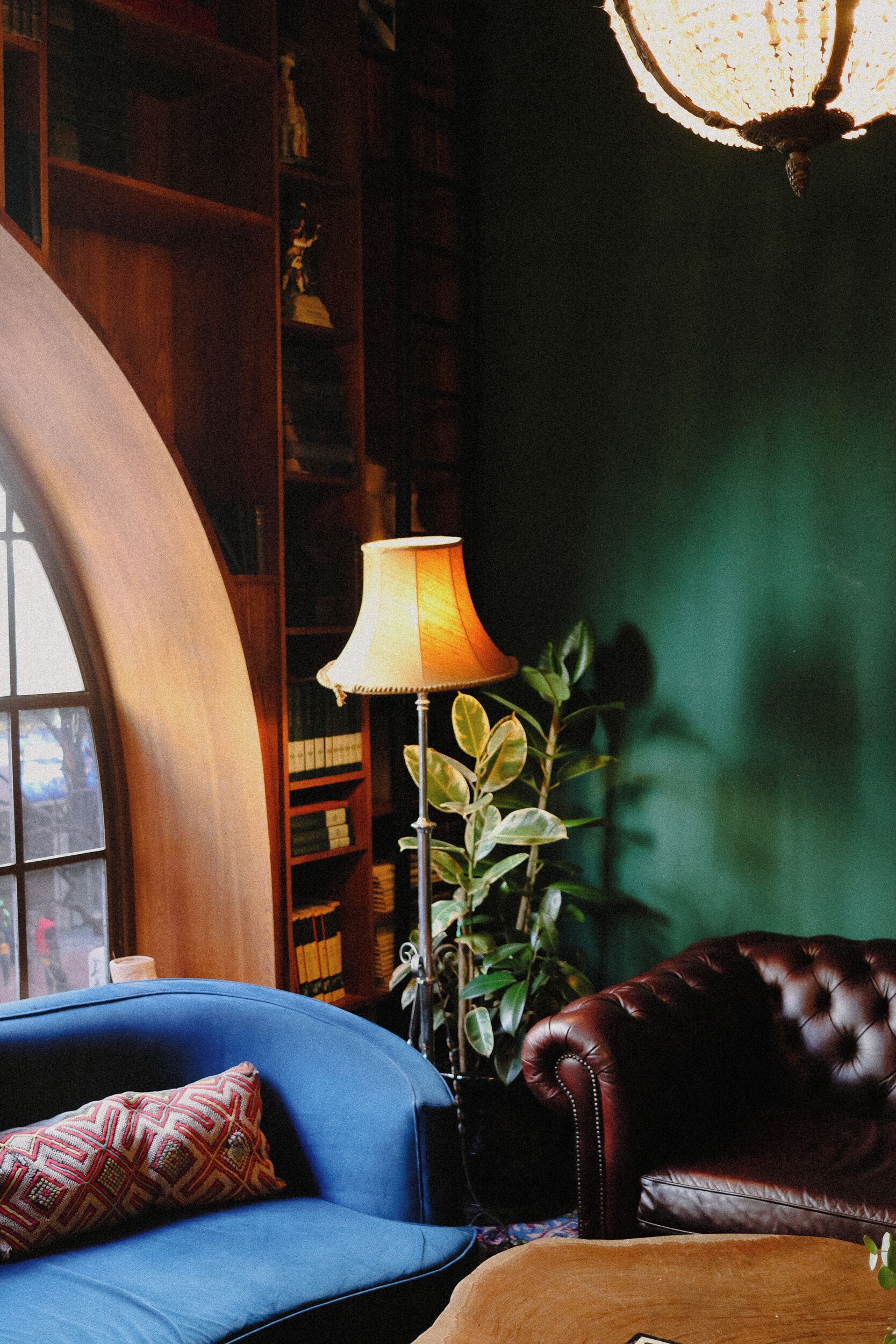 Una habitación con un sofá azul, un sillón de cuero, una estantería de madera y una lámpara de pie.
