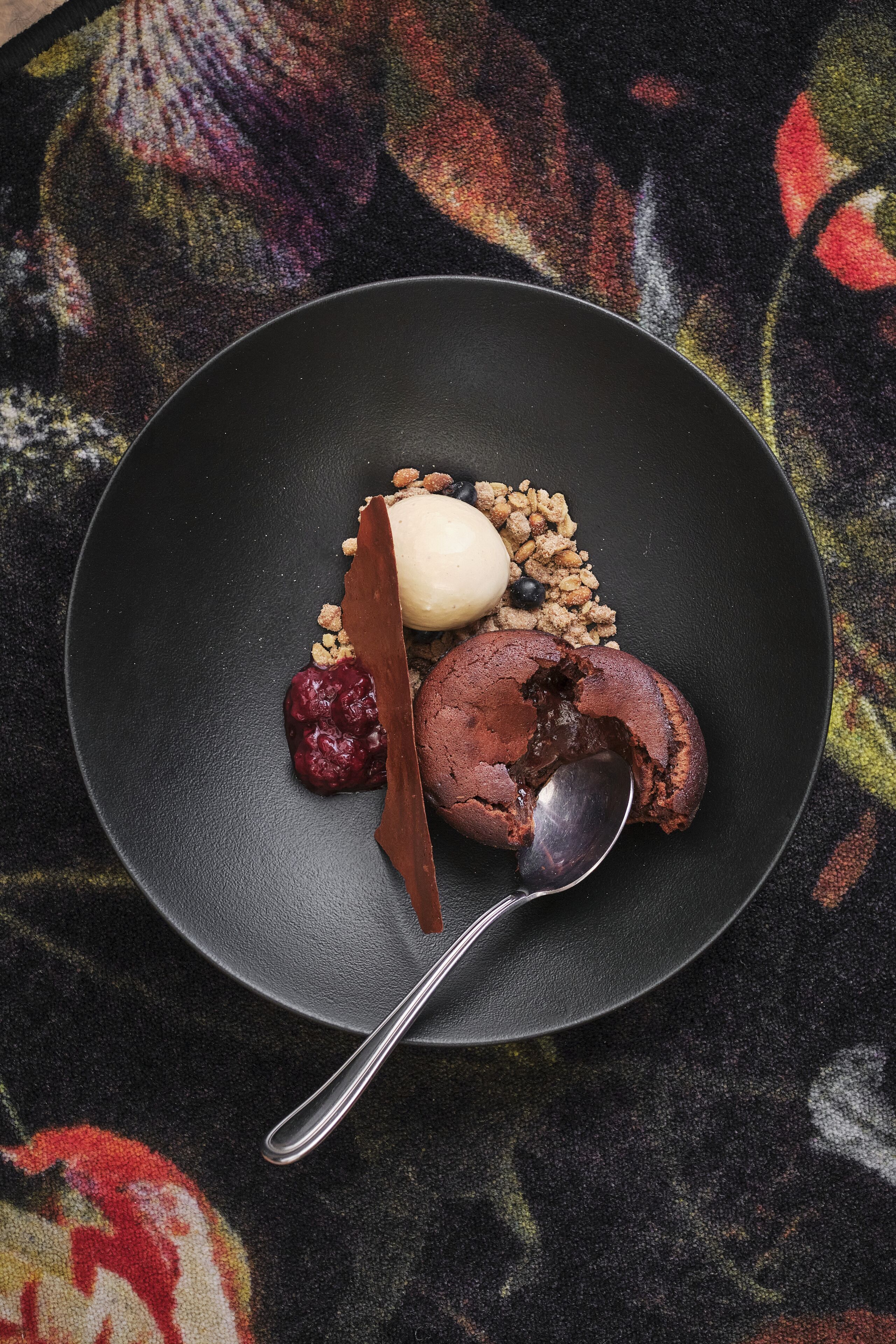 Een dessertbord met een bol ijs, een stuk chocoladetaart en een lepel.
