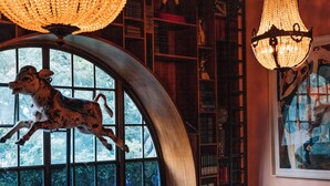 A cozy library with leather sofas, a large chandelier, and a unique arched window. - Gorgeous George by Design Hotels (Cape Town)