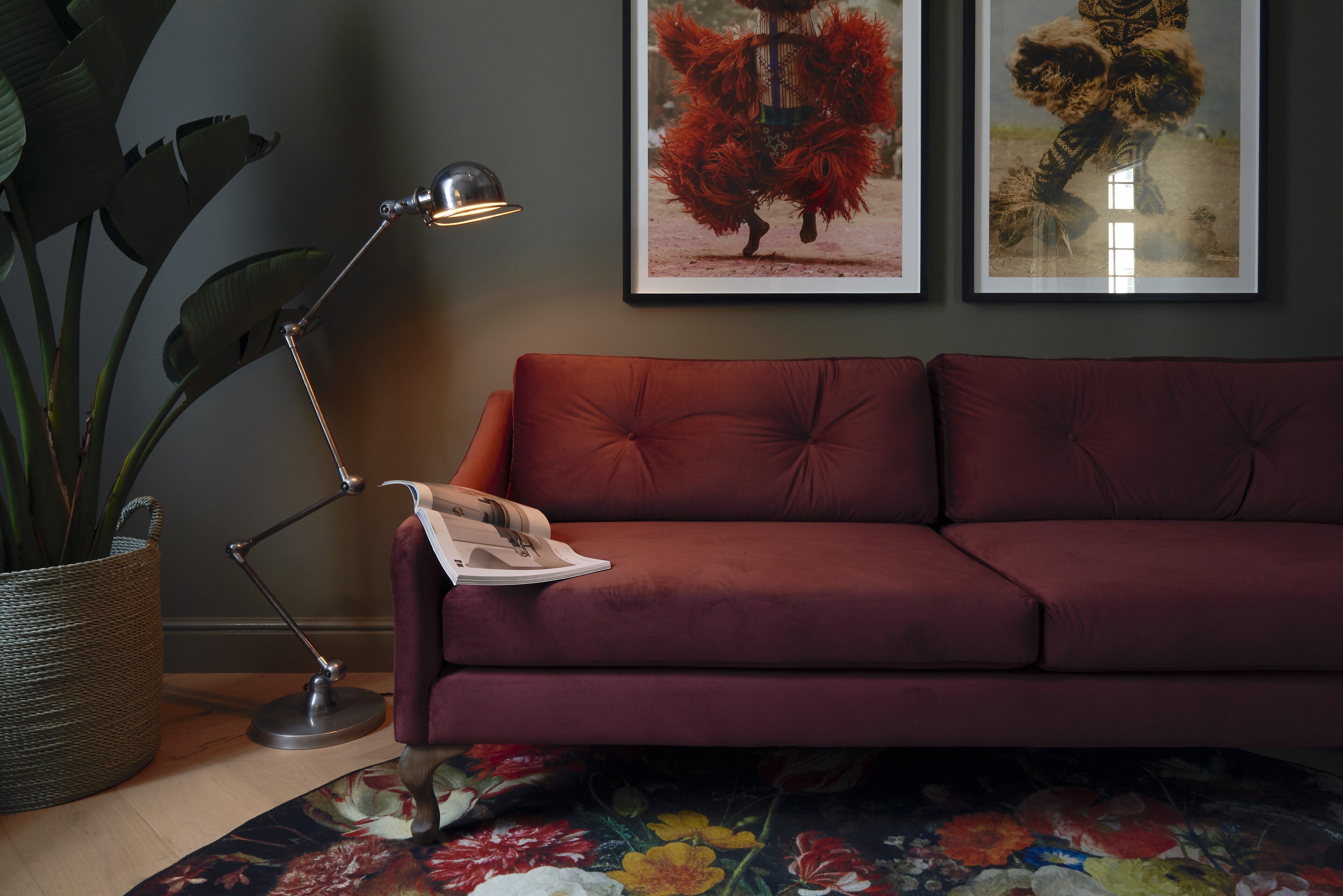 Une pièce avec un canapé rouge, un lampadaire, une plante en pot et deux tableaux encadrés accrochés au mur.