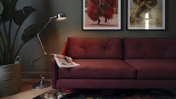 Une pièce avec un canapé rouge, un lampadaire, une plante en pot et deux tableaux encadrés accrochés au mur.