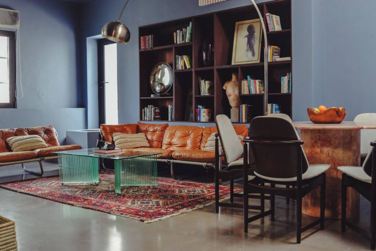 A modern living room with a leather sofa, a glass coffee table, and a bookshelf filled with books and decorative items.
