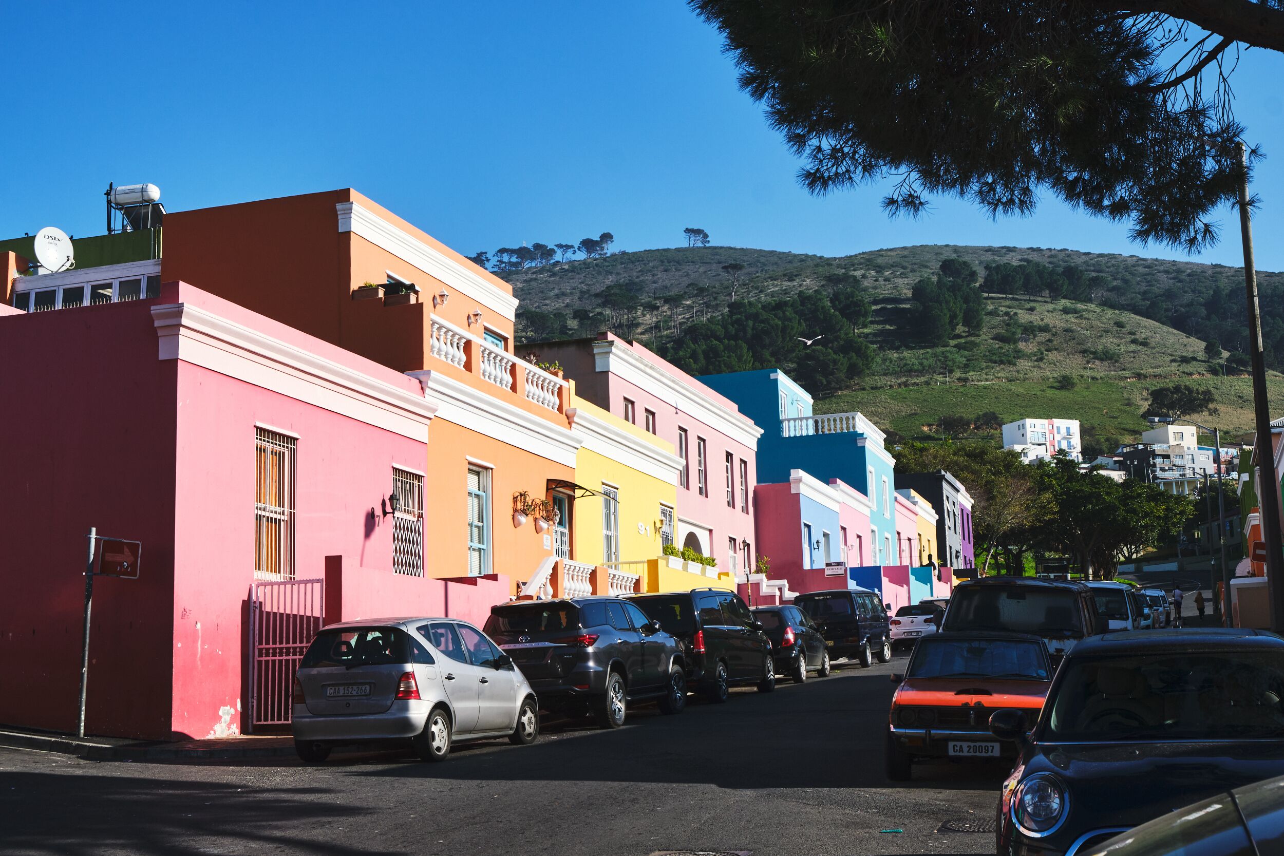 A row of colorful buildings with parked cars on a street.