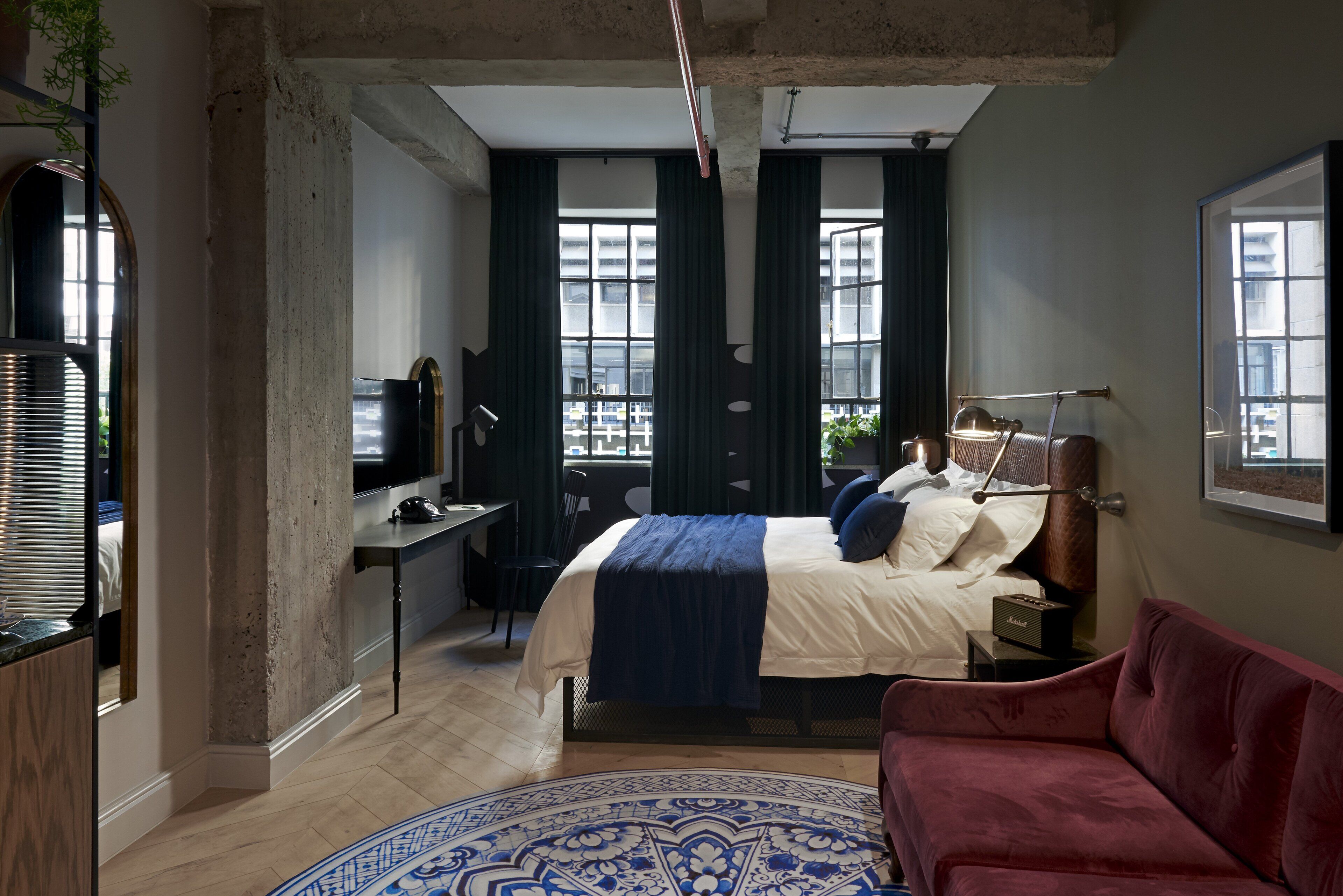 A modern bedroom with a bed, a desk, a red sofa, and a large window.