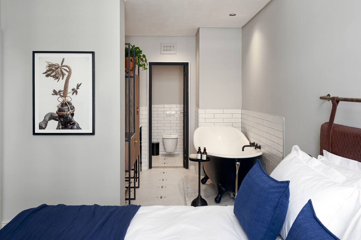 A modern hotel room with a bed, a bathtub, and a framed artwork on the wall.