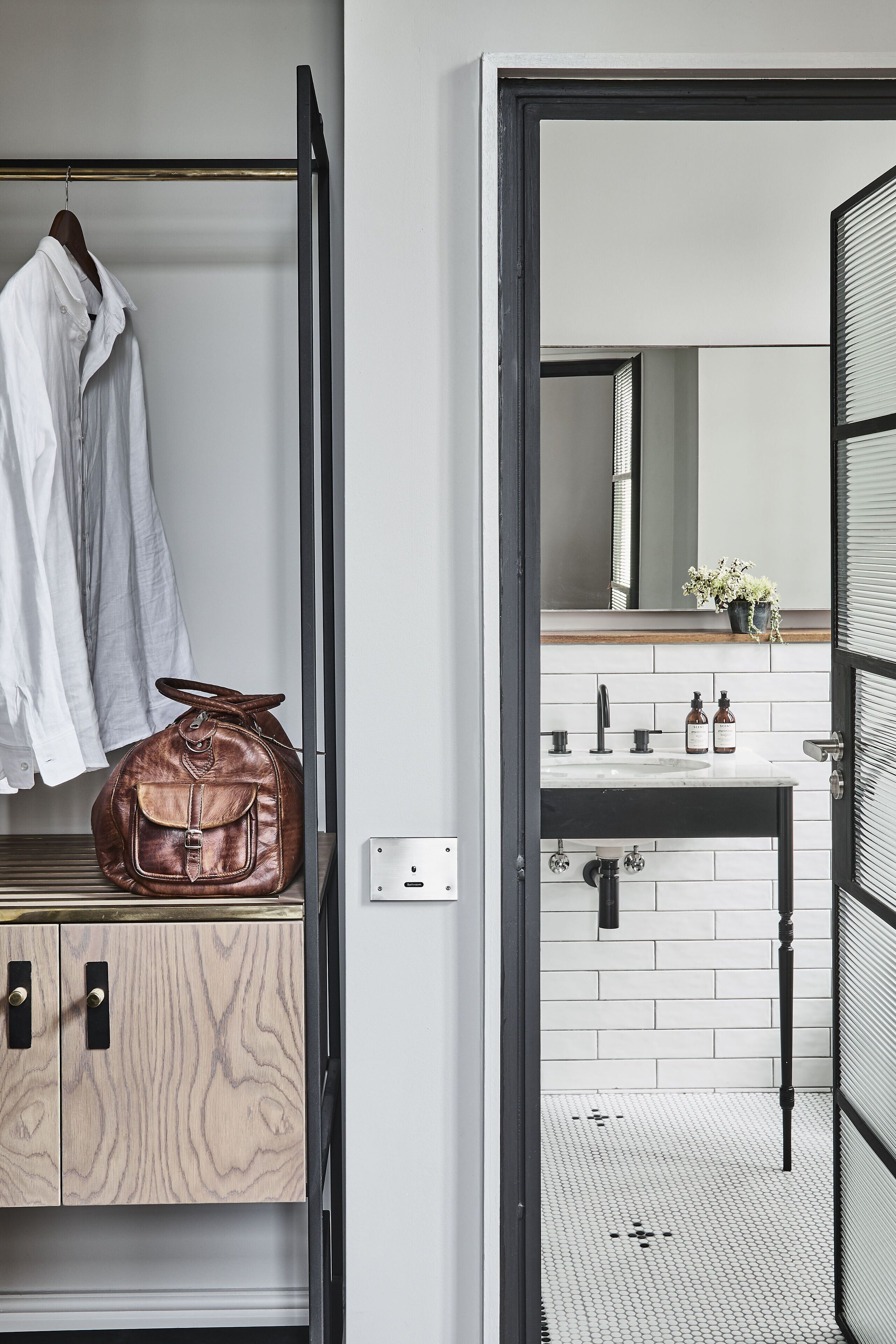 A modern bathroom with a white sink, black faucet, and a mirror above it. There is a brown leather bag on a wooden cabinet.