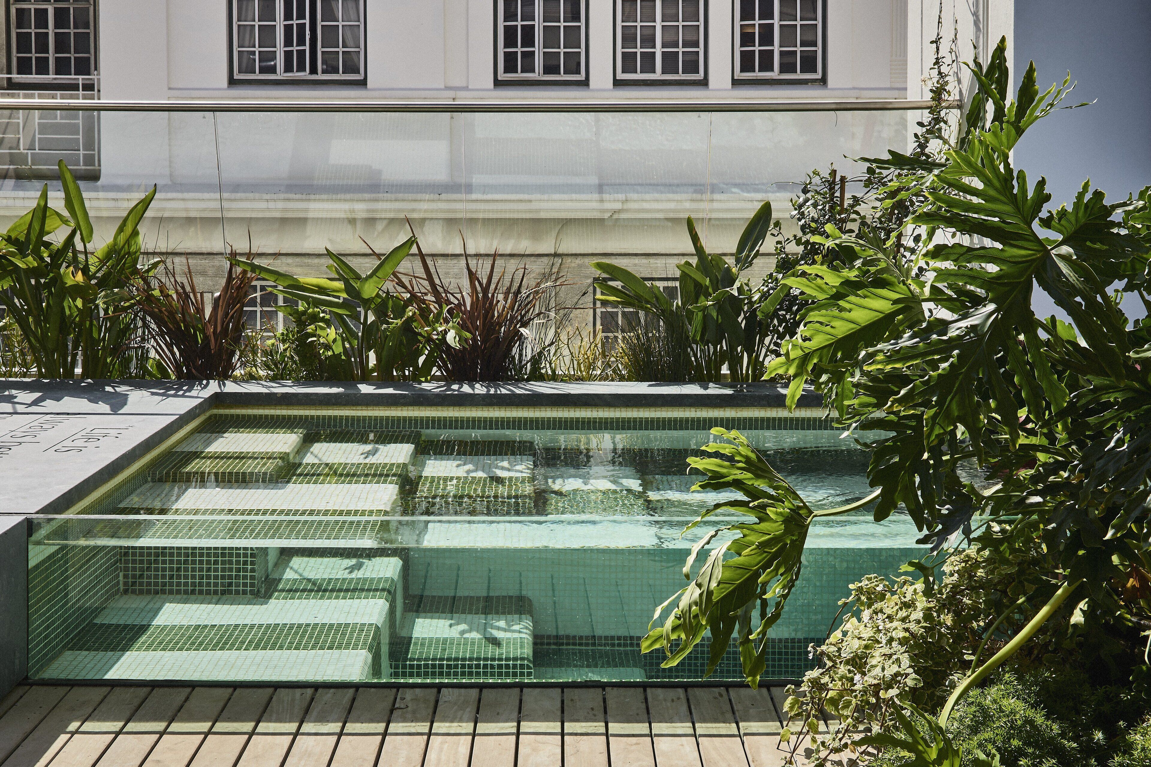 Ein rechteckiger Pool mit klarem Wasser, umgeben von üppigem Grün und einem Gebäude mit großen Fenstern im Hintergrund.