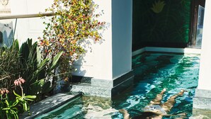A person in a swimming pool with a straw hat and a drink, surrounded by greenery and a decorative wall. - Gorgeous George by Design Hotels (Cape Town)
