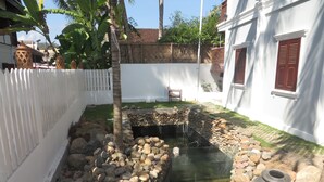 Un patio con un pequeño estanque, paredes blancas y una cerca blanca.