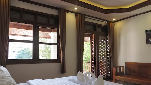 Habitación de hotel con una cama grande, cabecera de madera, un banco de madera y una ventana con cortinas.