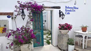 Un edificio blanco con una puerta turquesa, plantas en macetas y un letrero que dice "Boheme Bleue Konuk Evi Cafe".