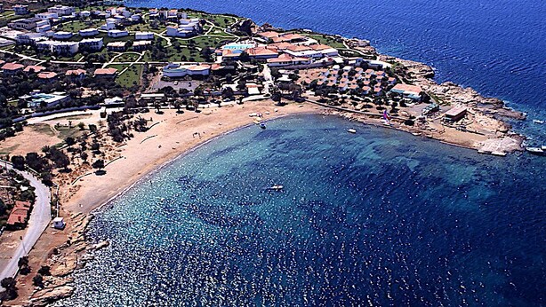 Vista aérea de un complejo turístico costero con villas, una playa y aguas azules cristalinas.