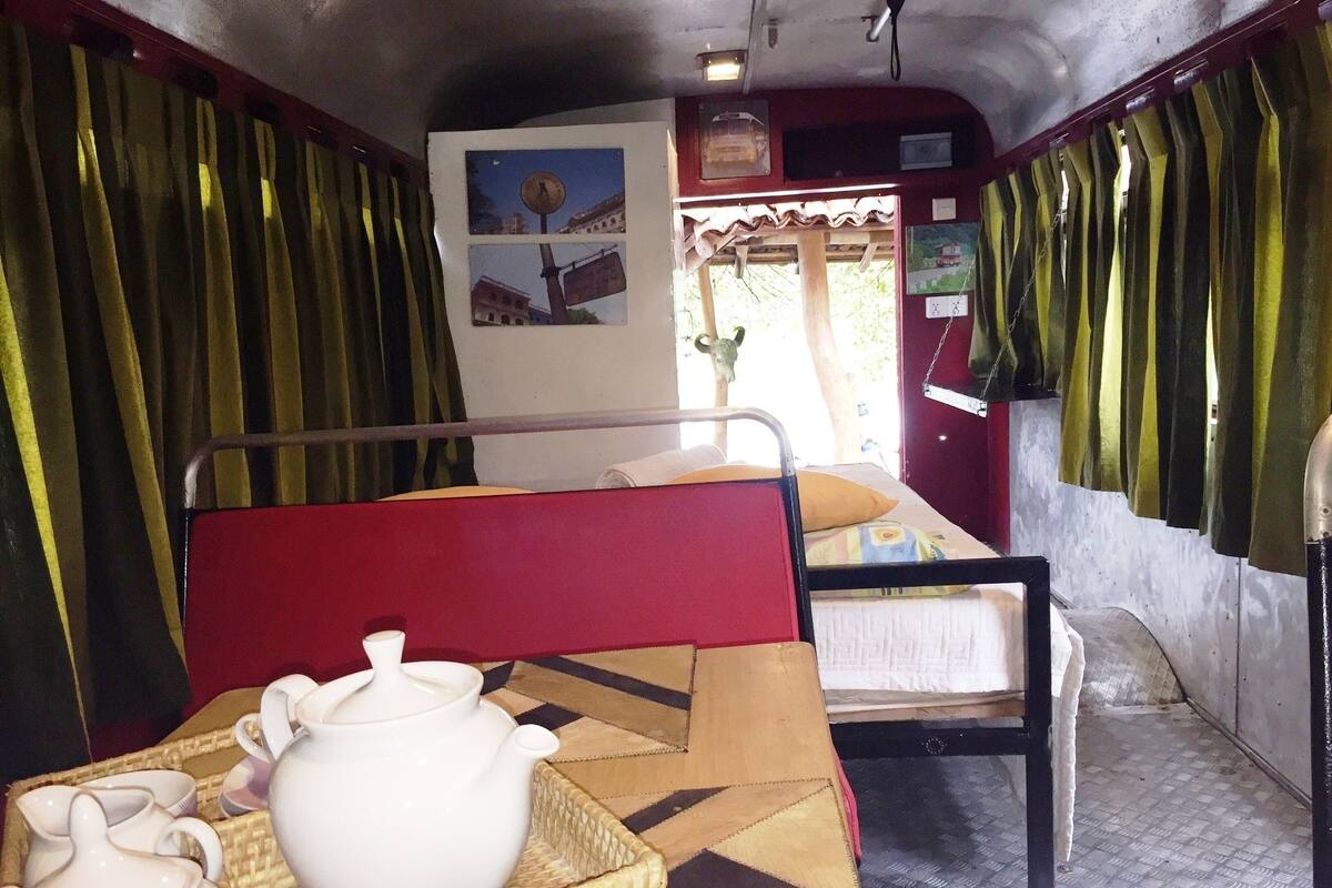 A compact room with a bunk bed, a table with a teapot and cups, and a wall with pictures.