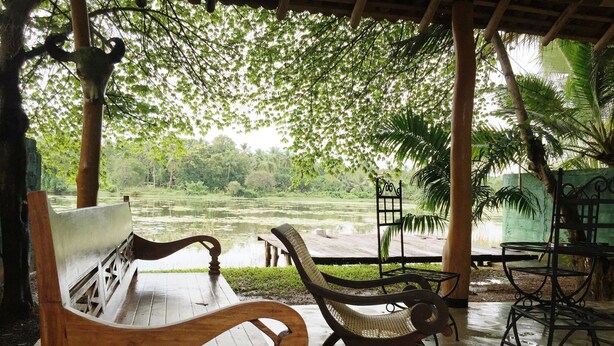 A wooden bench and a metal chair under a wooden structure with a view of a pond and surrounding greenery. - Mahawewa Nature Resort and SPA (Tangalle)