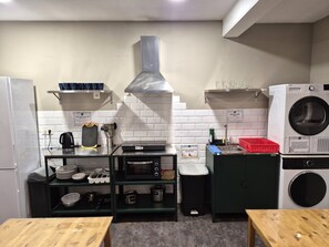 A compact kitchen with a microwave, toaster, sink, and a built-in washing machine. - Balea Hostel (San Sebastián)