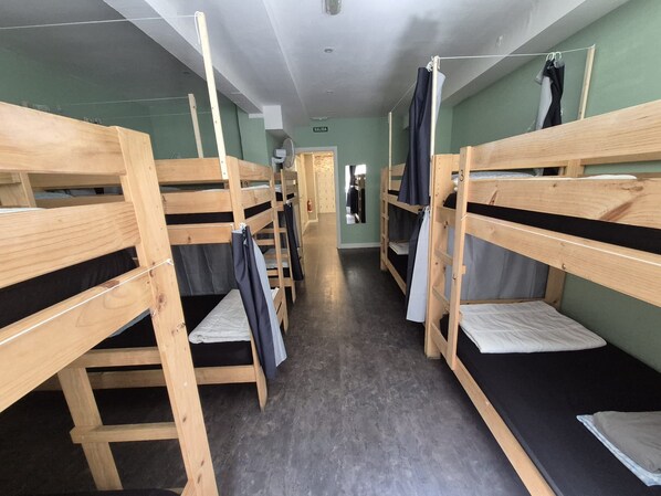 Une chambre de dortoir avec des lits superposés, un couloir et une porte marquée du mot « SORTIE ».