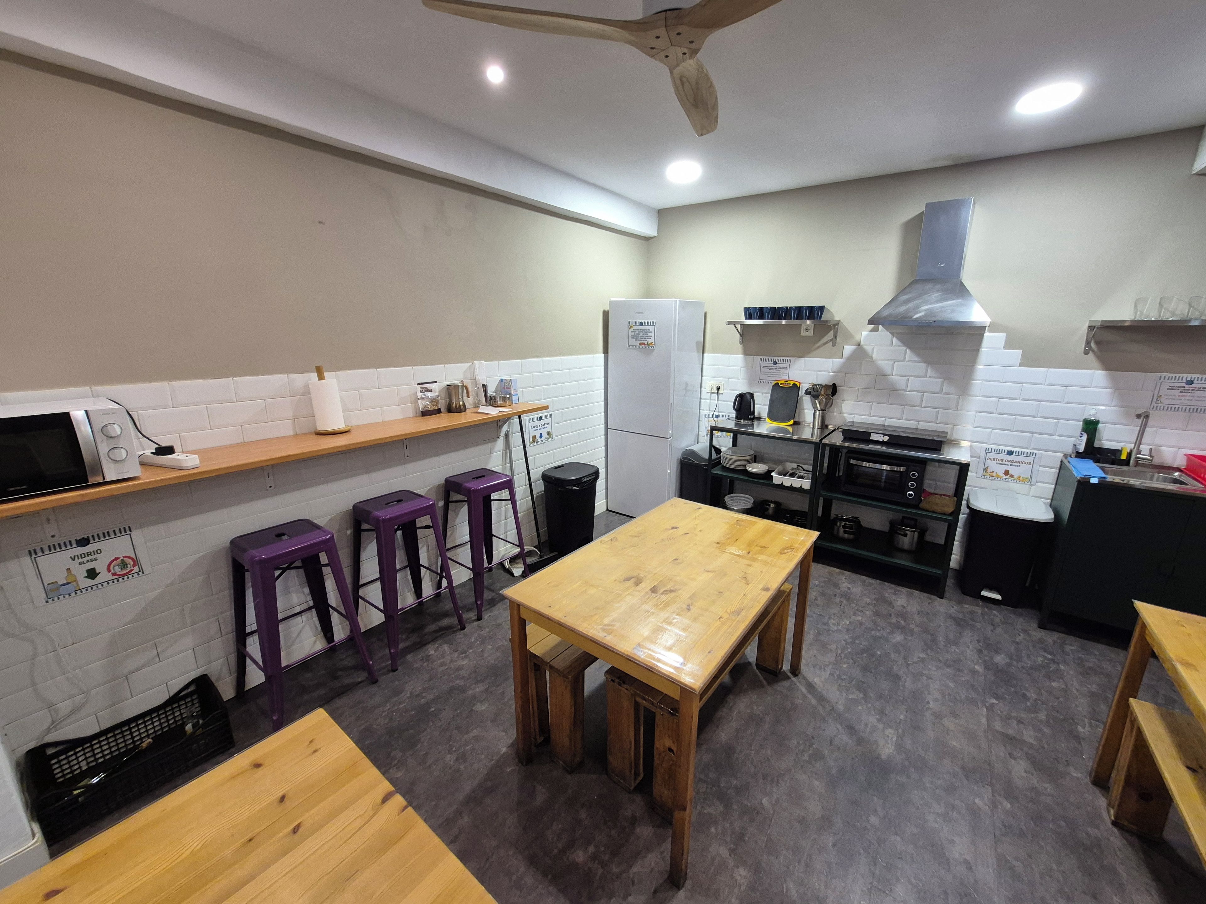 A compact kitchen with a wooden table, purple stools, a refrigerator, and a stove.