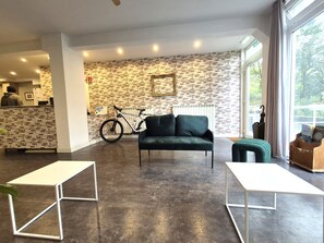 A modern interior with a brick-patterned wall, a green sofa, a bicycle, and a reception desk. - Balea Hostel (San Sebastián)