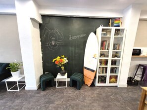 A room with a chalkboard, a surfboard, a bookshelf, and a small table with a plant. - Balea Hostel (San Sebastián)