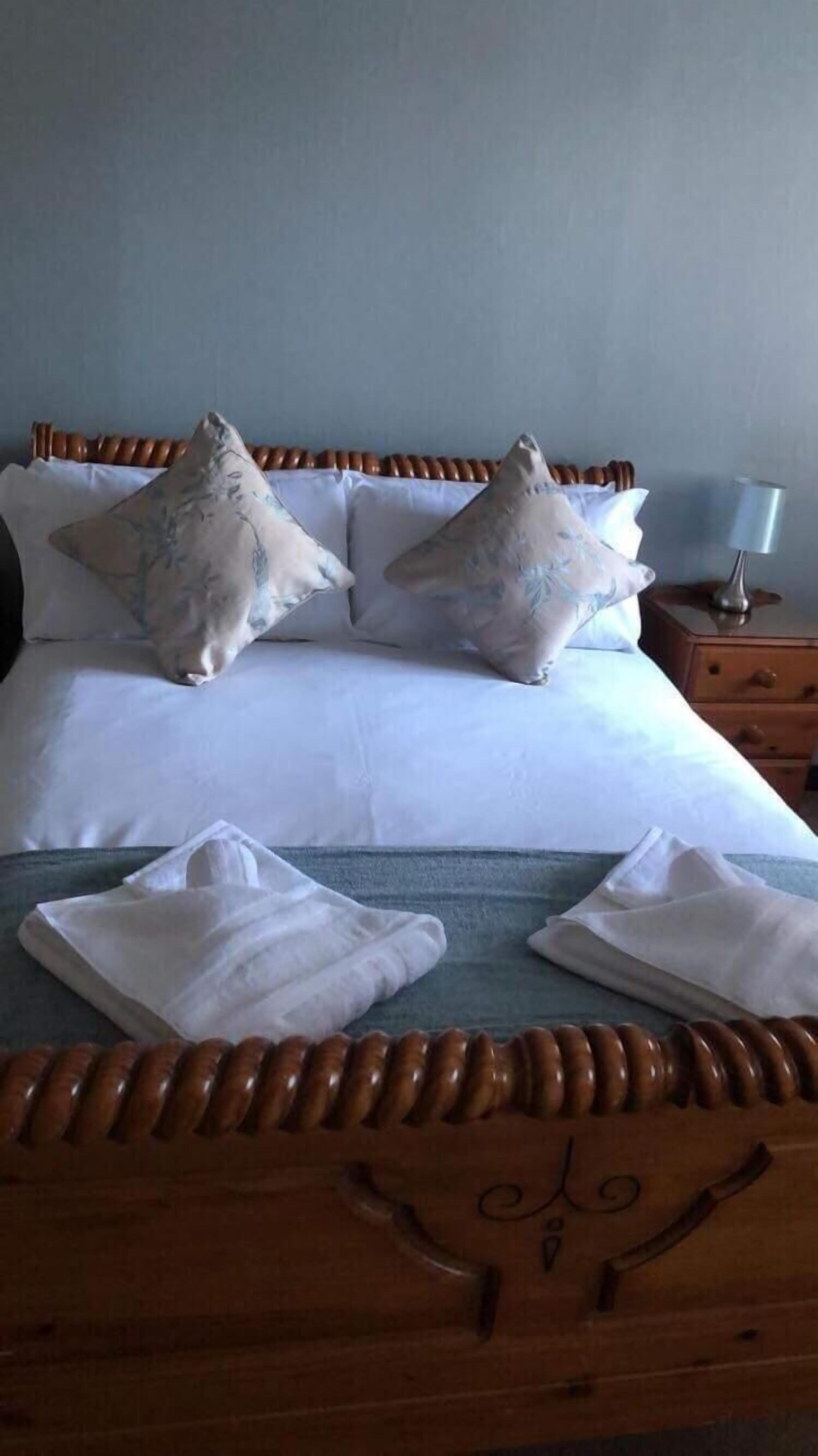 A neatly made bed with floral pillows, a wooden headboard, and a bedside table with a lamp.