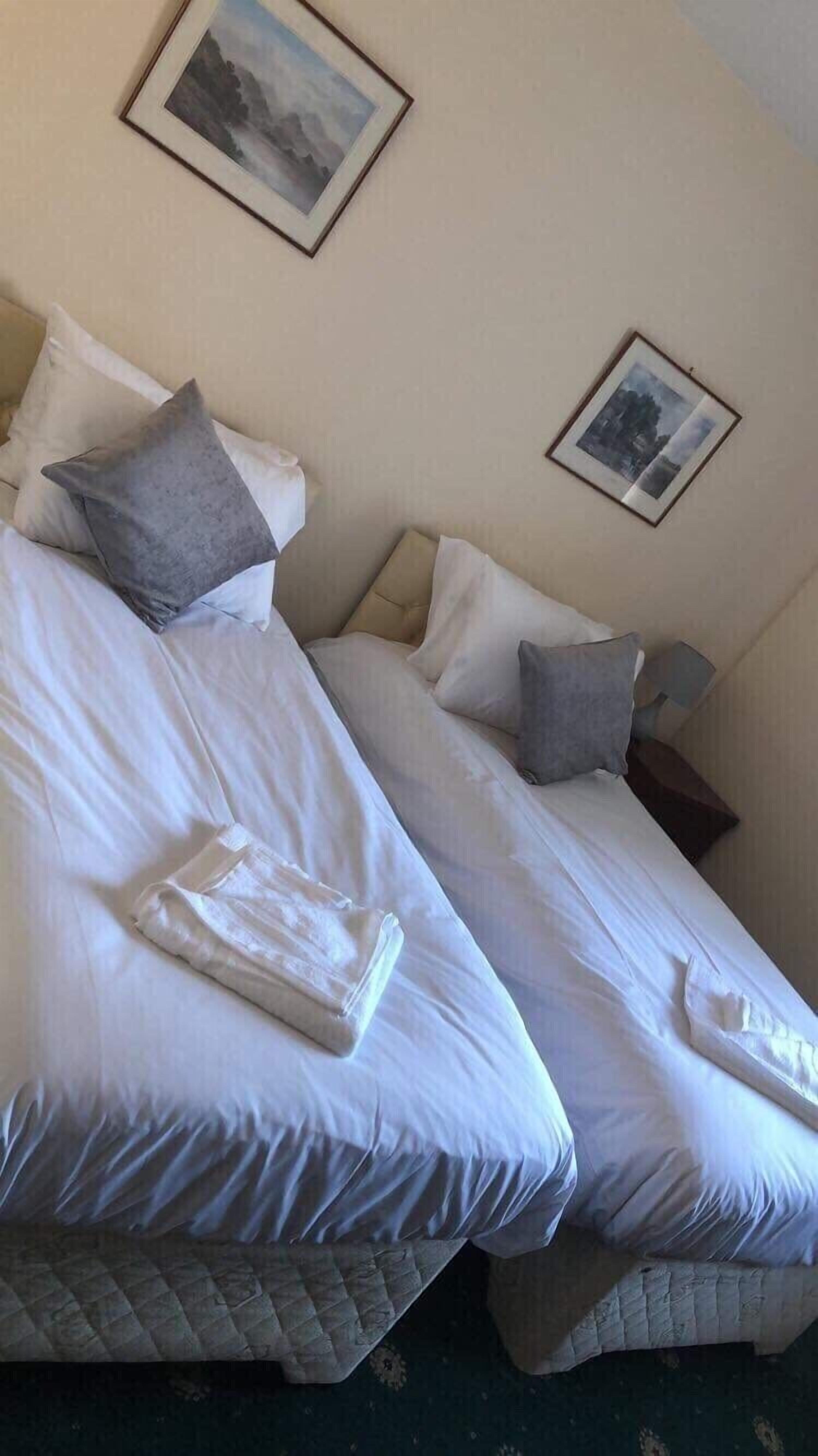 A hotel room with two beds, each with white linens and pillows, a quilted bedspread, and a framed picture on the wall.
