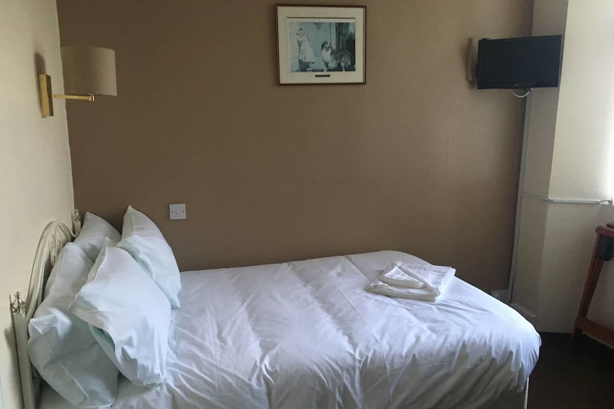 A single bed with white linens, a framed picture on the wall, and a television on the right.