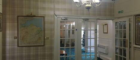 A hotel lobby with a chandelier, a map on the wall, and a Christmas tree visible through the glass doors.